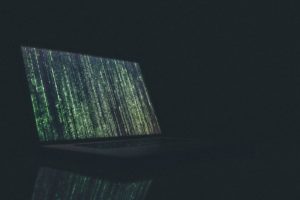 Ein Laptop ist in einem dunklem Raum zu sehen, auf dem Bildschirm ist Code aufgerufen. Ein Hacker will Ransomware verbreiten. Bild: Unsplash/Markus Spiske