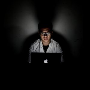 Zu sehen ist ein Mann in einem dunklen Raum. Licht, erzeugt durch einen Laptop-Bildschirm, fällt auf das Gesicht des Mannes. Vielleicht ist er ein Hacker und die Cyber-Abwehr proaktiv macht ihm Angst. Bild: www.unsplash.com / 广博 郝