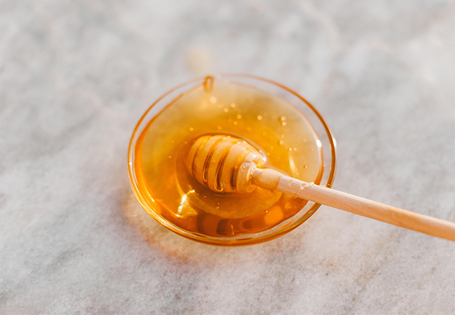 Zu sehen ist eine Glasschale mit Honig auf einem marmorierten Hintergrund. Der Honigtopf steht sinnbildlich für Honeypot. Bild: Pexels/Roman Odintsov