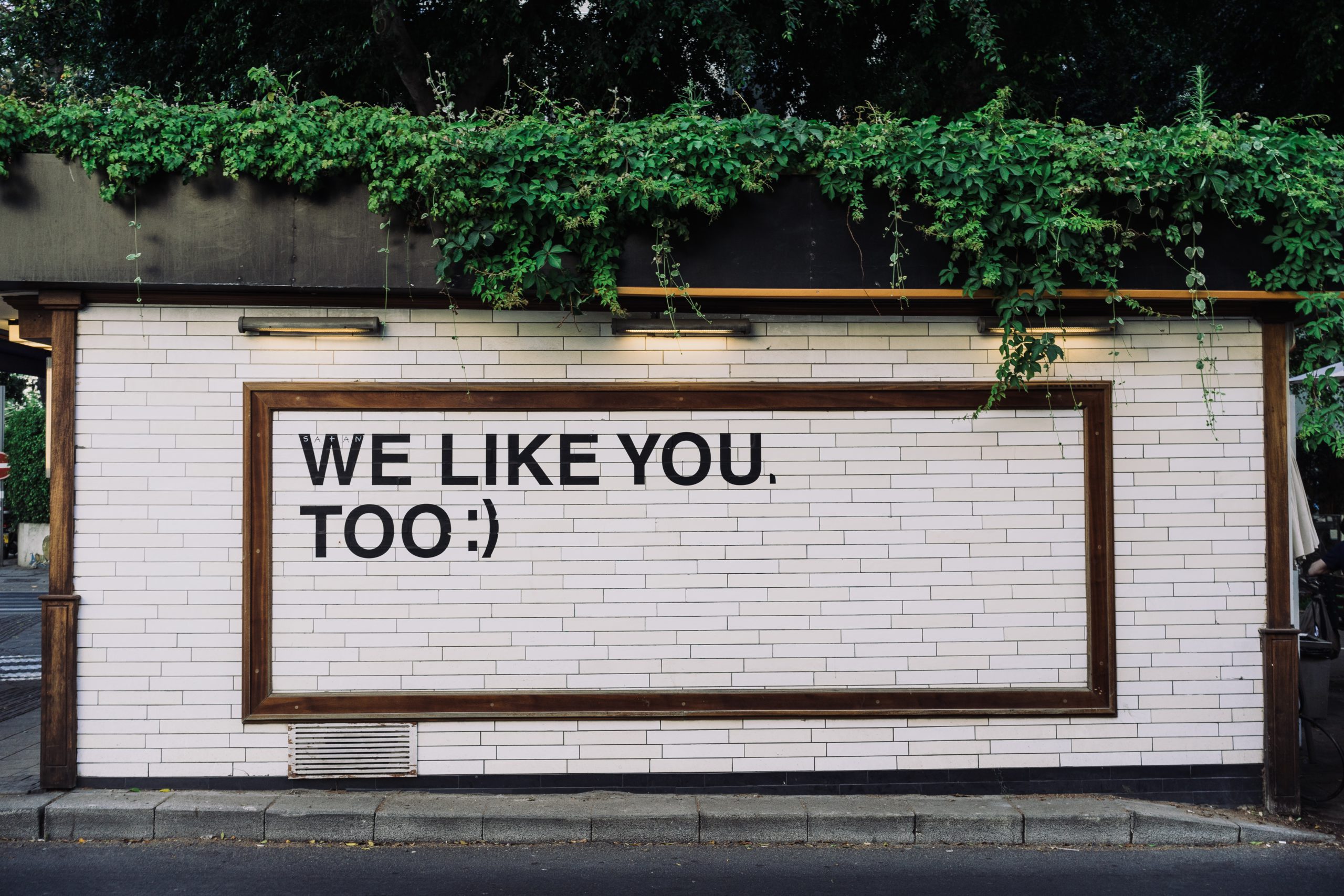 Das Bild zeigt eine Wand auf der der Spruch „Wie Like You. Too.“ steht. Sie symbolisiert das Problem mit Paid Likes und dass eine „Gefällt Mir“-Angabe längst nicht mehr aussagekräftig ist. Bild: Unsplash/Adam Jang