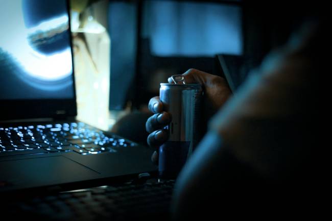 Zu sehen ist eine Person mit Energy-Dring in dunkler Umgebung vor einem Laptop. Ein Qakbot-Hacker? Bild: Pexels/Sai Krishna