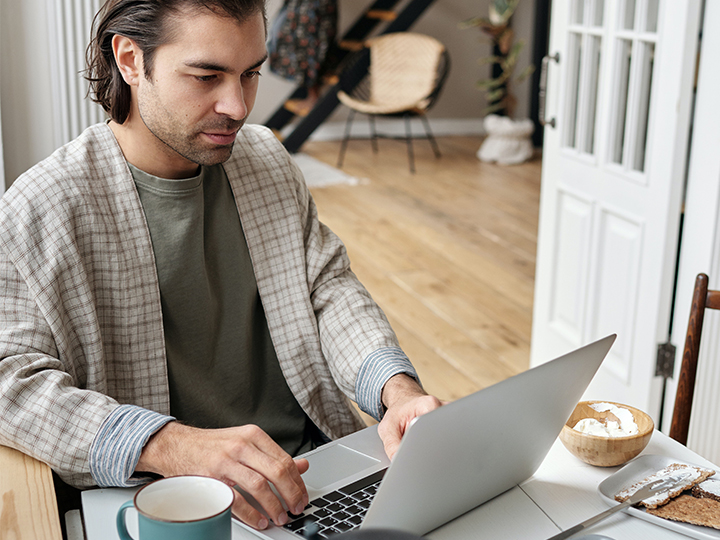Ein Mann sitzt am Frühstückstisch im Home Office am Laptop. Phishing-Mail-Beispiele zeigen durch eine geringere Aufmerksamkeit im Home Office Erfolg. Bild: Pexels/Jack Sparrow