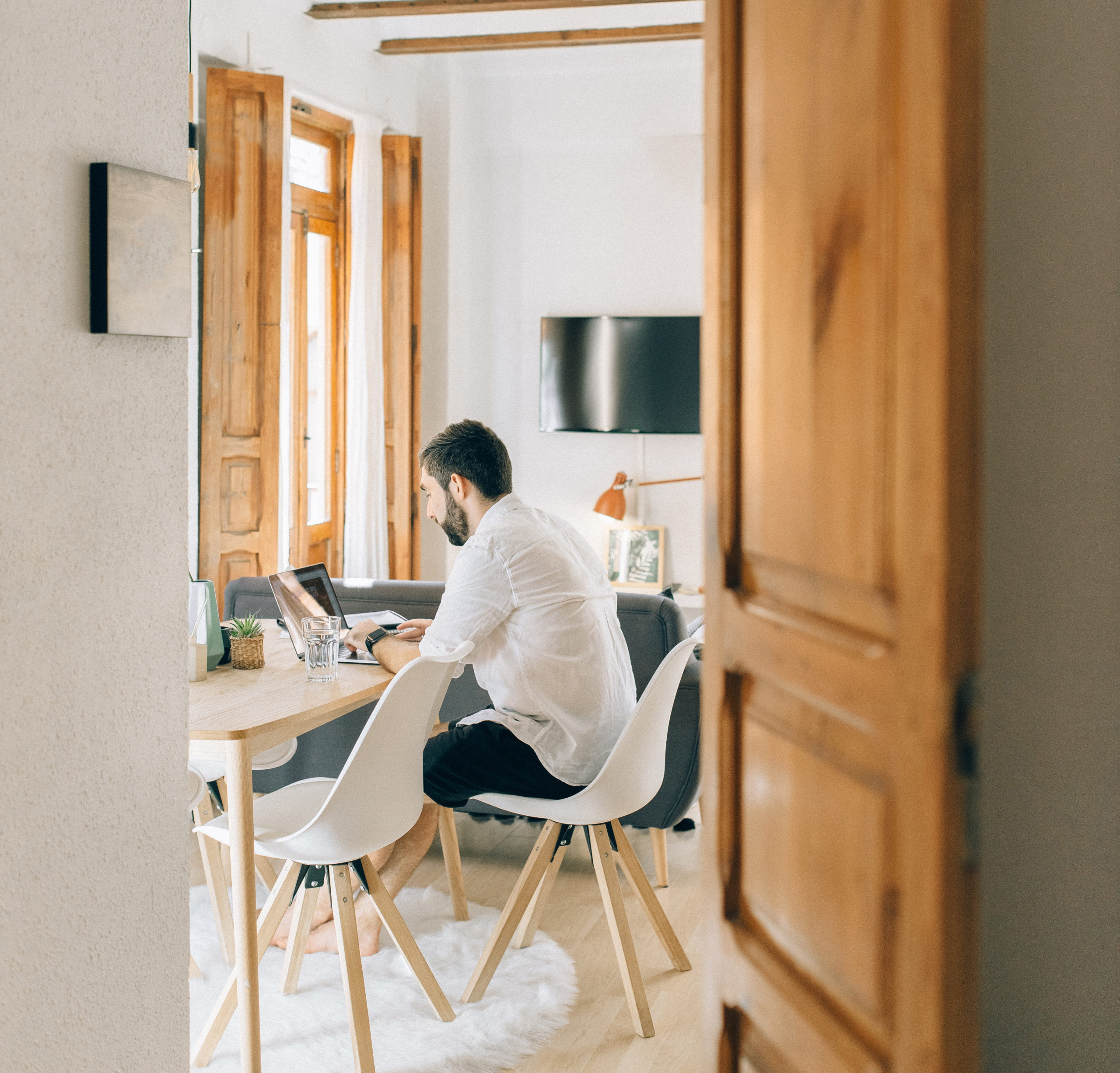 Durch eine Tür sieht man einen Mann mit seinem Laptop am Esstisch arbeiten. Mitarbeiter überwachen im Home Office ist aktuell ein Thema. Bild: Pexels / Nataliya Vaitkevich