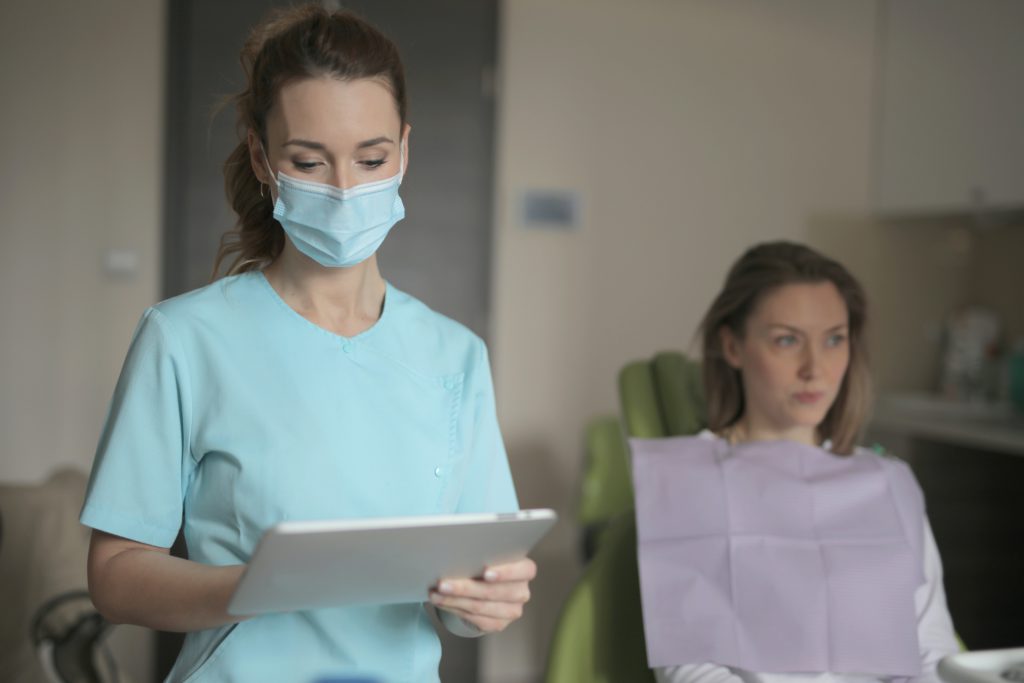 Eine Zahnärztin schaut auf ein Tablet, auf dem sie die elektronische Patientenakte einsehen kann. Eine Patientin sitzt auf dem Behandlungsstuhl. Bild: Pexels/Andrea Piacquadio