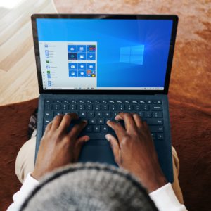 Aus der Vogelperspektive ist ein Mann mit Mütze und einem Laptop auf den Knien zu sehen. Er will keine der veralteten Windows-10-Versionen nutzen und upgraden. Bild: Unsplash/Windows