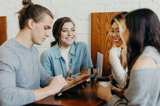 Vier Kollegen, drei Frauen und ein Mann, arbeiten in lockerer Runde zusammen und haben Spaß. hier wird Feel-Good-Management gelebt. Bild: Unsplash/Brooke Cagle