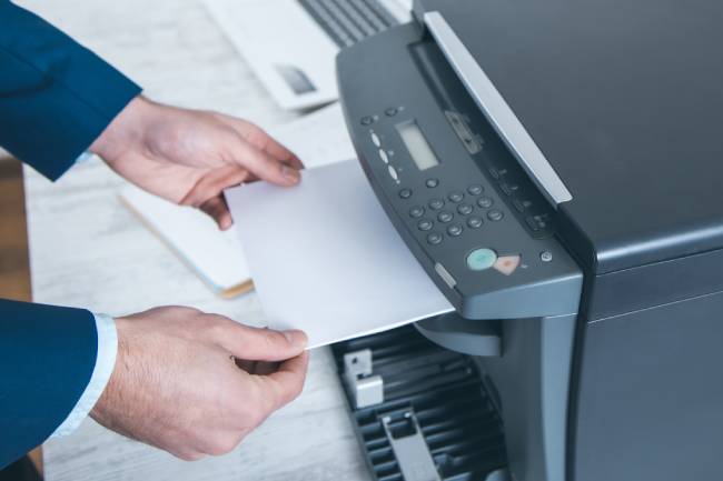 Zu sehen, sind Hände, die ein Fax aus einem Multifunktionsdrucker entnehmen. Problem für den Datenschutz: Faxe können in die falschen Hände geraten. Bild: stock.adobe.com/ARAMYAN
