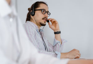 Ein IT-Experte trägt ein Headset und spricht während der Fernwartung mit dem PC-Nutzer. Bild: Pexels/Mart Production