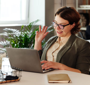 Eine Frau winkt bei einer beginnenden Videokonferenz in die Kamera ihres Laptops. Sie nutzt Live-Untertitel. Bild: Pexels/Marcus Aurelius