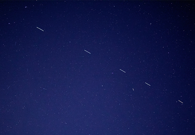 Zu sehen ist der Nachthimmel mit Sternen und Starlink-Satelliten mit Bewegungsunschärfe. Bild: Unsplash/Forest Katsch 