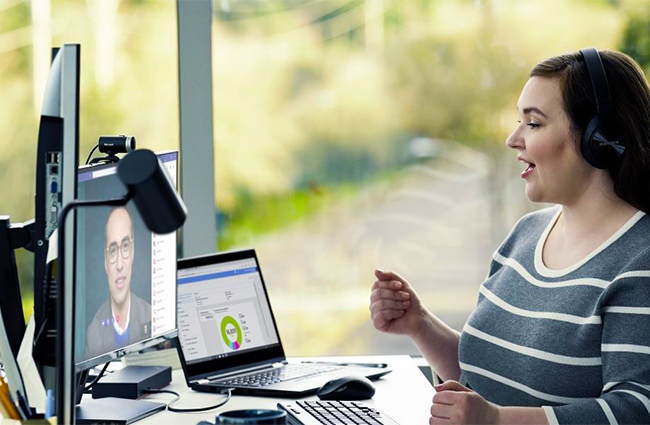 Eine Frau sitzt in einer Videokonferenz am PC und nutzt Office-Programme. Sie freut sich auf Office 2021. Bild: Microsoft