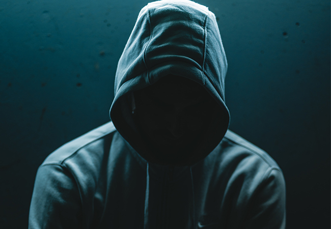 Zu sehen ist ein Mann mit Kapuzenpulli und verborgenem Gesicht; er steht symbolisch für die Anonymität der Hackergruppe REvil. Bild: Unsplash/Philipp Lansing