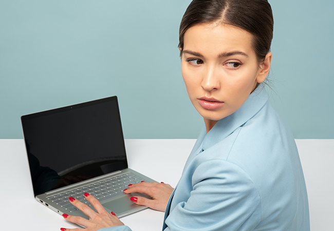 Zu sehen ist eine Frau am Laptop, die auf der Hut ist und über ihre Schulter schaut. Ein Fall von Sabotage in Unternehmen? Bild: Unsplash/Icons8 Team