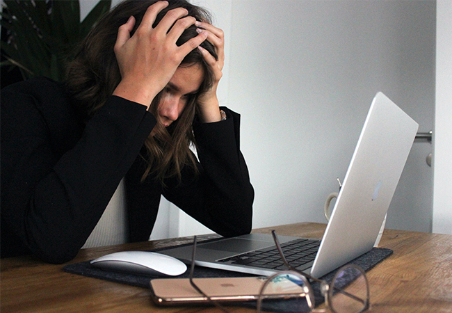 Ein Frau sitzt am Laptop und schlägt die Hände über dem Kopf zusammen. Vielleicht ist sie auf eine Attacke hereingefallen. Bild: Unsplash/Elisa Ventur