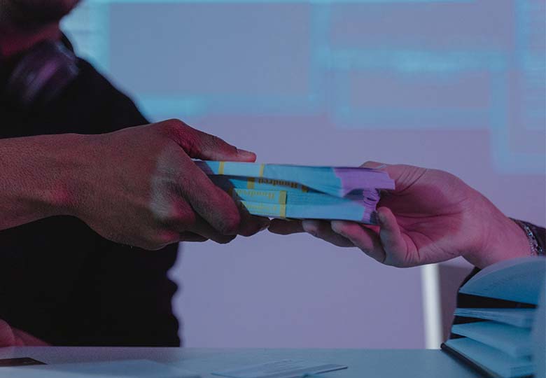 Eine Hand übergibt ein Bündel Geldscheine einer anderen Hand. Der Datenhandel floriert im Darkweb. Bild: Pexels/Tima Miroshnichenko