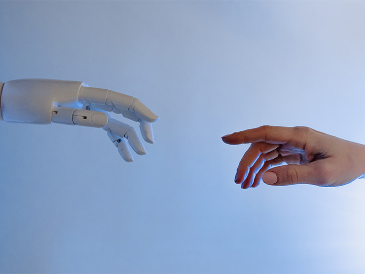 Eine Roboter-Hand und eine menschliche Hand bewegen sich mit jeweils ausgestrecktem Zeigefinger auf einander zu. Bild: Pexels/Tara Winstead
