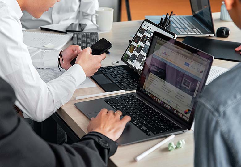 Zu sehen ist ein Konferenztisch mit vielen Laptops und Händen, die die Laptops bedienen. Alle Geräte sind per Endpoint Security geschützt. Bild: Pexels/Mikhail Nilov