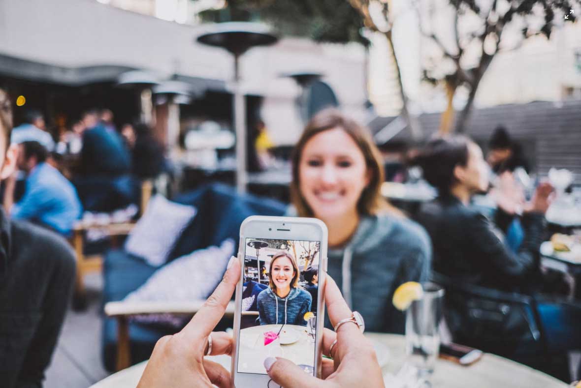 Zwei junge Frauen sitzen in einem Cafe und die eine fotografiert die andere mit dem Smartphone, um das Foto in den sozialen Median zu posten. Thema ist der Datenschutz im Internet. Bild: Unsplash/Josh Rose