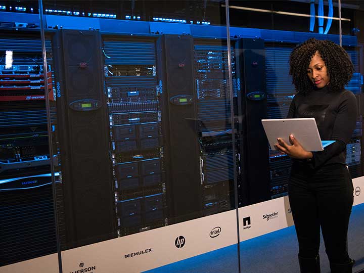 zu sehen ist eine Frau mit einem Laptop in einem Server-Raum. Thema ist der Data Protection Report 2022.