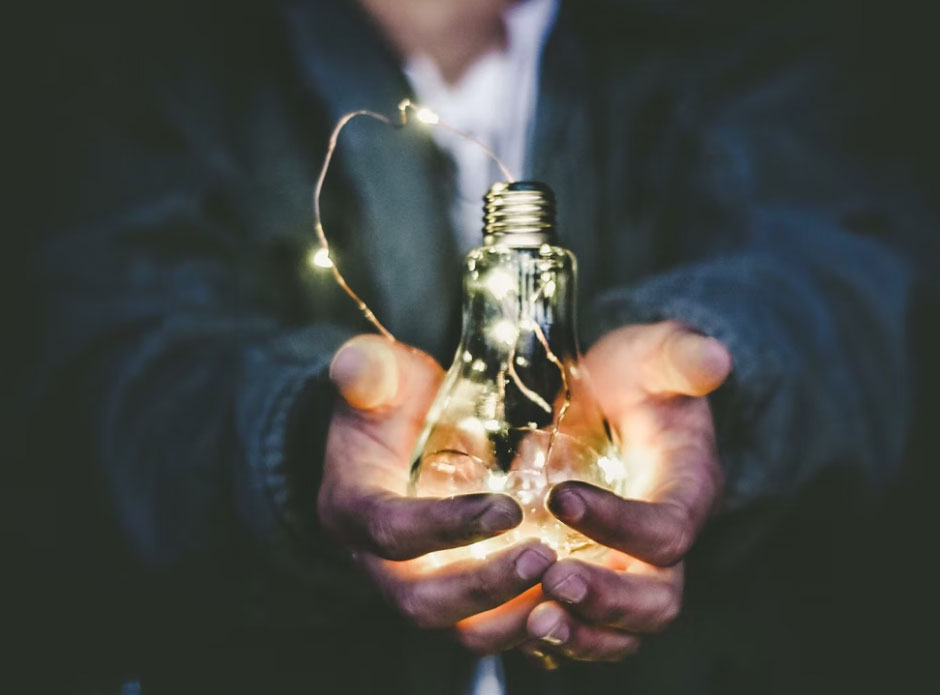 zu sehen ist ein Mann, der eine Glühbirne in den Händen hält. Thema ist die Frage, wie Energiekosten im Unternehmen reduziert werden können. Bild: Unsplash/Riccardo Annandale