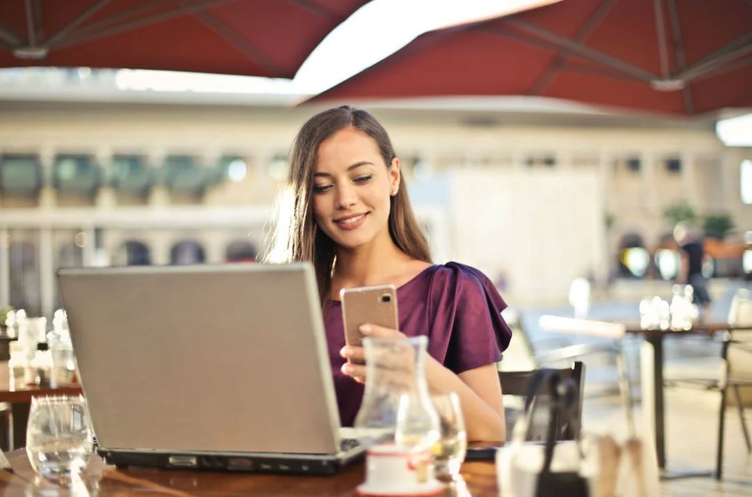 zu sehen ist eine Frau mit Laptop und Smartphone in einem Straßencafe. Thema ist der Cyber Resilience Act. Bild: Pexels/Andrea Piacquadio