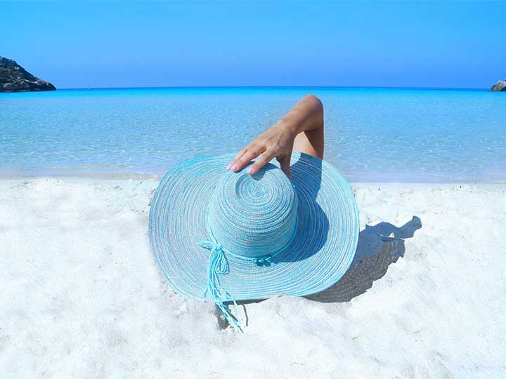 zu sehen ist eine Frau mit einem Sonnenhut von hinten, die an einem Strand liegt. Das Thema sind die Brückentage 2023. Bild: Pexels/Pixabay