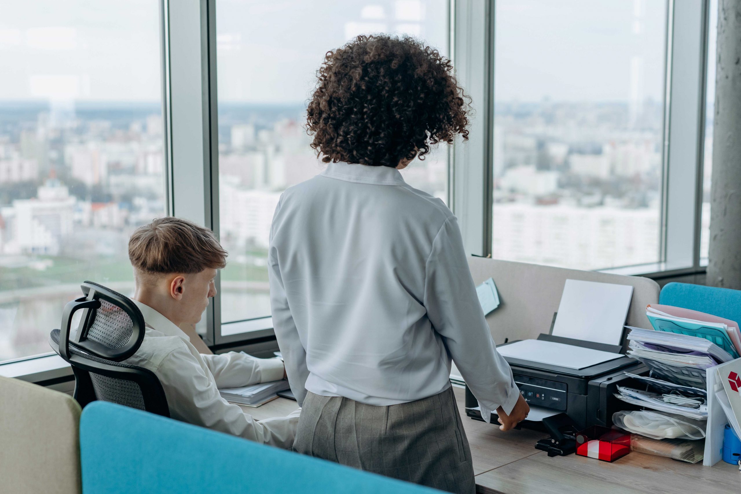 zu sehen sind zwei Büro-Angestellte vor einem Schreibtisch mit einem Drucker drauf. Bild: Pexels/Mikhail Nilov