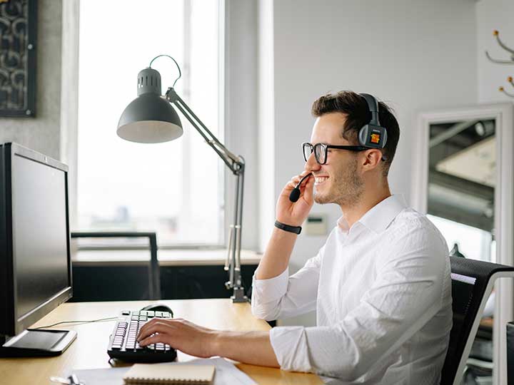 Telefonanlage für kleine Unternehmen. Zu sehen ist ein Mann an seinem Arbeitsplatz, der ein Headset trägt und über die Cloud telefoniert. Bild: Pexels/Yan Krukov
