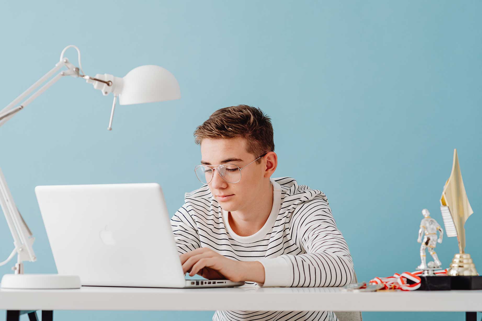 zu sehen ist ein Junge im Teenager-Alter, der mit seinem Laptop an seinem Schreibtisch im Jugendzimmer sitzt. Das Thema sind Script-Kiddies, also jugendliche Amateur-Hacker. Bild: Pexels/Karolina Grabowska