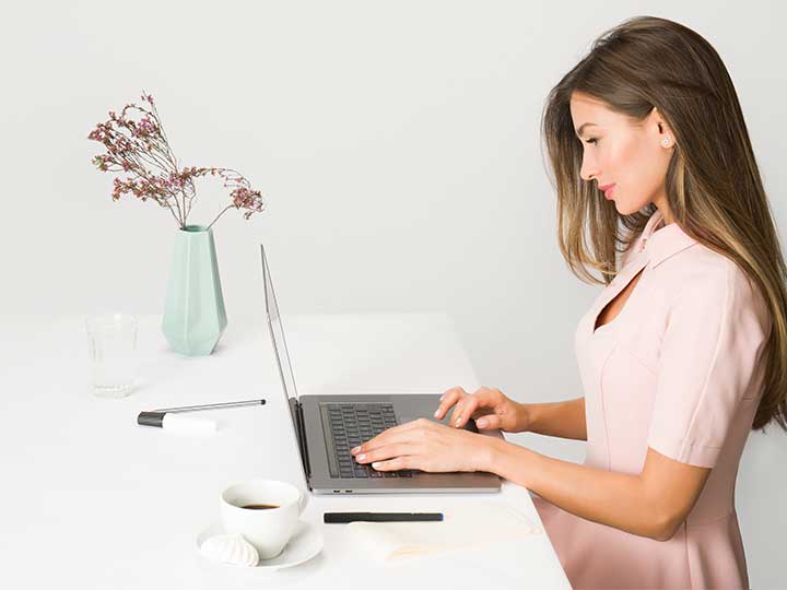 zu sehen ist eine lächelnde Frau am Schreibtisch vor ihrem Laptop. Bild: Pexels/Moose Photos
