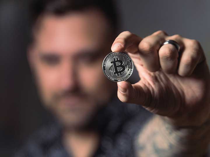 ein im Hintergrund verschwommen dargestellter Mann zeigt eine Bitcoin Münze ist die Kamera. Thema ist die Hardware-Wallet zur Erhöhung der Sicherheit beim Handel mit Kryptowährungen. Bild: Pexels/Crypto-Crow