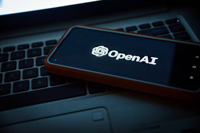 Zu sehen ist ein HAndy, das auf einer Laptop-Tastatur liegt und auf dem das Logo von OpenAi zu sehen ist. Als Entwickler muss sich OpenAI Fragen zu KI und Datenschutz gefallen lassen. Bild: Unsplash/Levart_Photographer