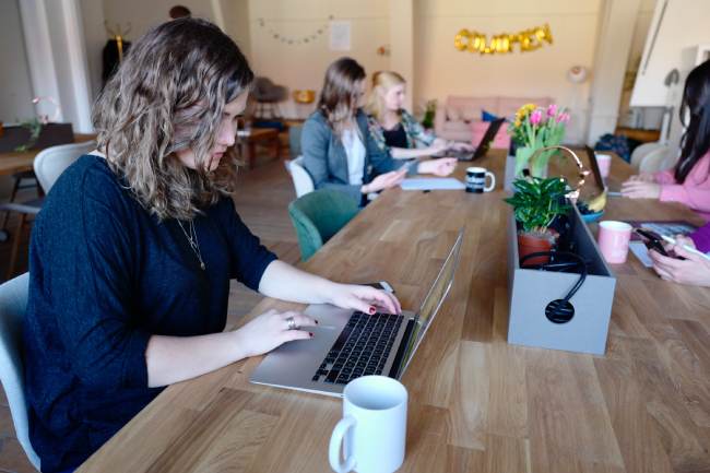 Zu sehen ist ein großer Tisch in einem Coworking Space für Frauen in Berlin, an dem fünf Frauen jede für sich arbeiten. Bild: Unsplash/CoWomen