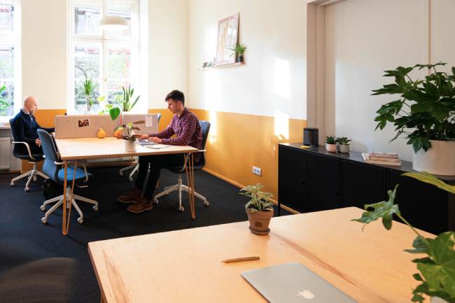 Zu sehen ist ein Coworking Space; im Hintergrund arbeiten zwei Personen jeweils an einem Schreibtisch. Bild: Unsplash/Yolk CoWorking - Krakow