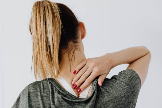 Zu sehen ist der Rücken einer Frau; sie hält sich mit der Hand den Nacken. Sie leidet unter mangelnder Ergonomie am Arbeitsplatz. Bild: Pexels/Karolina Grabowska