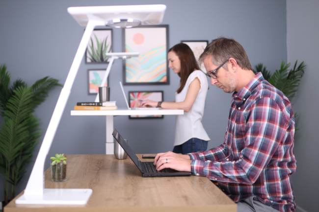 Ein Mann und eine Frau arbeiten jeweils am Laptop an einem höhenverstellbaren Schreibtisch. Dieser unterstützt die Ergonomie am Arbeitsplatz. Bild: Unsplash/TheStandingDesk