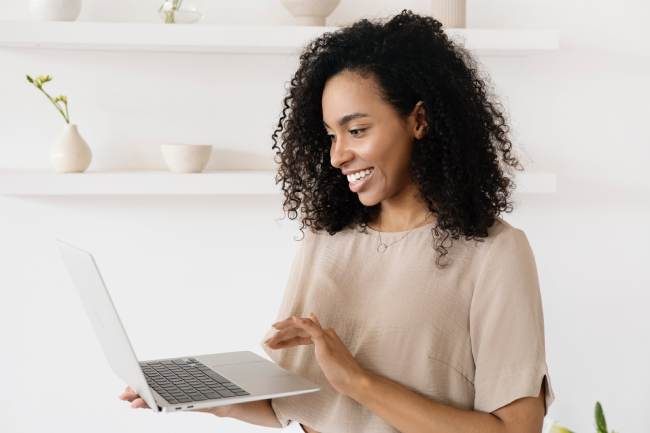 Zu sehen ist eine fröhliche Frau mit Laptop. Sie hat dank Netiquette eine angenehme Online-Konversation. Bild: Pexels/Anna Nekrashevich