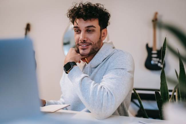 Ein Mann sitzt lächelnd am Laptop und scheint einen angenehmen Kommunikationspartner zu haben. Beide halten sich vermutlich an die Netiquette. Bild: Pexels/William Fortunato