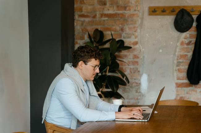 Zu sehen ist ein Mann am Laptop. Er verwendet eine professionelle E-Mail-Signatur. Bild: Pexels/MART PRODUCTION