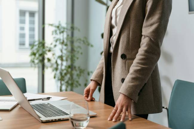 Zu sehen ist der Oberkörper einer Frau in Anzug stehend vor ihrem Laptop auf dem Tisch. Es geht um CEO-Fraud. Bild: Pexels/MART PRODUCTION 