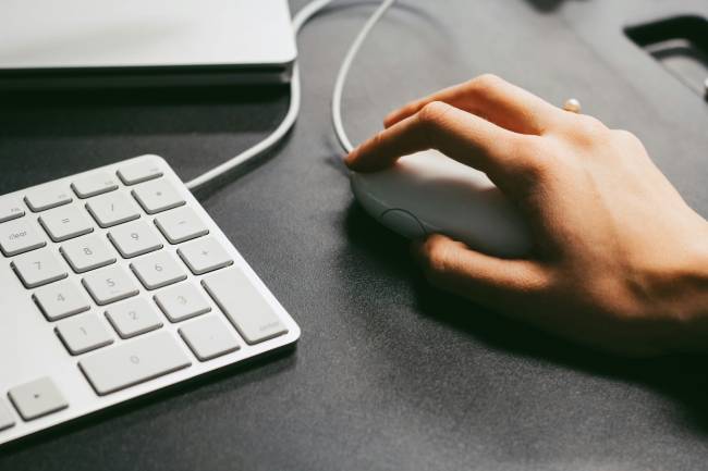 Zu sehen sind eine Hand, die eine Maus bedient, eine Tatstatur und ein Laptop. Es geht um den Digital Operational Resilience Act. Bild: Pexels/Maria Stewart.