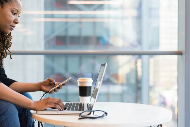 Zu sehen ist eine Frau mit Laptop und Handy, vielleicht macht sie einen kurzen E-Mail-Check. Bild: Unsplash/Christina @ wocintechchat.com