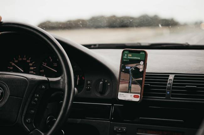 Zu sehen ist die Innenansicht eines Autos mit Lenkrad und Smartphone mit Google Maps. Das Handy sammelt hier Standortdaten für das Standort-Tracking. Bild: Pexels/Isaac Mehegan