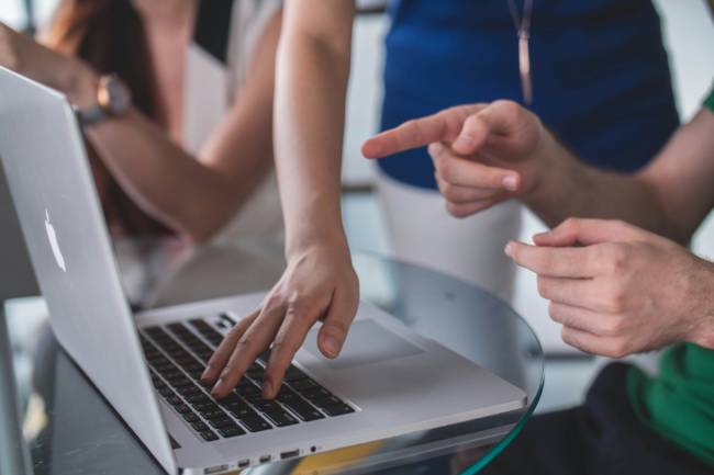 Zu sehen ist eine Person, die einer anderen etwas am Laptop zeigt. Vielleicht eine Schulung zur KI-Kompetenz? Bild: Unsplash/Mimi Thian