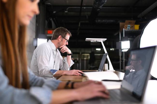 Zu sehen ist eine Büroszene, eine Frau und ein Mann arbeiten an ihren Laptops. Ob sie KI-Kompetenz haben? Bild: Unsplash/TheStandingDesk