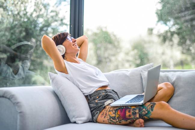 Zu sehen ist eine lachende Frau Zuhause auf ihrer Couch mit einem Laptop die womöglich gerade ihre mentale Stärke im Home Office trainiert. Bild: Pexels/Andrea Piacquadio