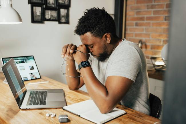 Zu sehen ist ein erschöpfter Mann Zuhause vor dem Laptop der seine mentale Stärke im Home Office trainieren sollte. Bild: Pexels/Tima Miroshnichenko