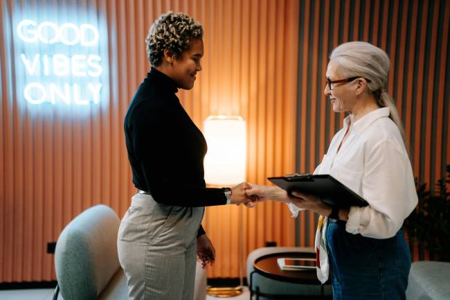 Zu sehen sind zewi Frauen, die sich die Hände geben. Womöglich ist es eine Vorgesetze mit ihrer Mitarbeiterin, die sich auf Augenhöhe im Rahmen begegnen, da im Unternehmen agiles Personalmanagement gelebt wird. Bild: Pexels/cottonbro studio