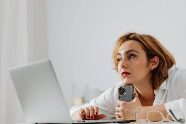Zu sehen ist eine Frau an einem Laptop und mit Smartphone in der Hand die wahrscheinlich gerade ein Fake Profil von Führungskräften entdeckt. Bild: Pexels/Kaboompics.com