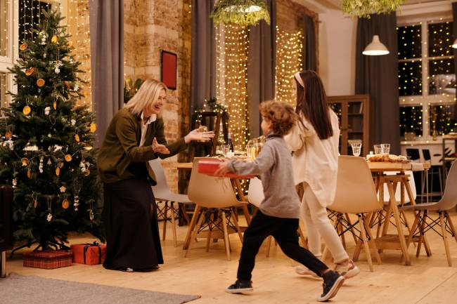 Zu sehen ist eine Frau mit zwei Kindern vor dem Weihnachtsbaum was den Weihnachtsurlaub mit gut geplanten Brückentagen 2026 symbolisieren soll. Bild: Pexels/Nicole Michalou